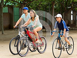 Cheerful family of three cycling on city road