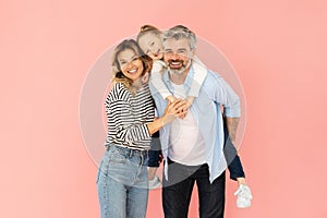 Cheerful Family Of Three Embracing Standing Over Pink Background