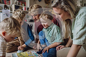 Cheerful family with three kids reading book in living room, on floor.