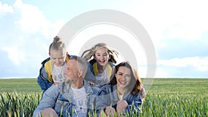 Cheerful family walks through a green field of wheat. Parents hold children by the hands.