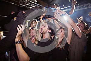 Cheerful fans lifting male performer at nightclub