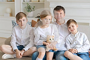 Cheerful father with laughing children looking at camera sitting on couch