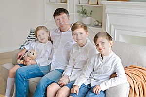 Cheerful father with laughing children looking at camera sitting on couch