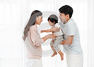 cheerful father and mother lifting and playing with toddler baby on white window background. happy family