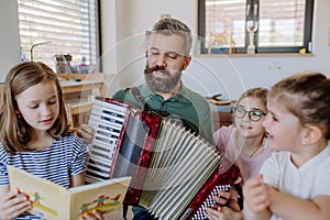 Cheerful father musician playing the accordion to his three little daughters at home.