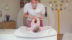 Cheerful father plays baby in room. He fits legs girl, he swings hands