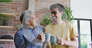 Cheerful father and son toasting coffee mugs while spending leisure time in kitchen at home