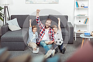 cheerful father with sons raising hands while watching soccer match