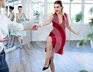 Cheerful woman in red practicing vigorous swing with man at dance class photo