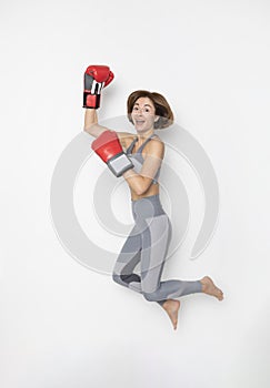 Cheerful female boxer in sportswear and boxing gloves jumping and flying  on white background