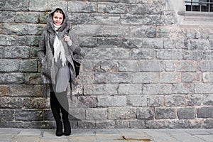 Cheerful female in coat hood near wall