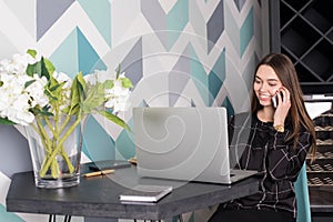 Cheerful female content manager calling via cellphone and using net-book