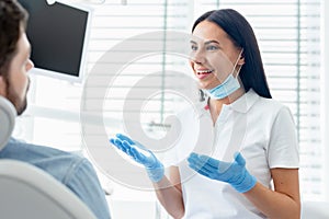 Cheerful female dentist advicing and gesturing to patient in modern clinic photo