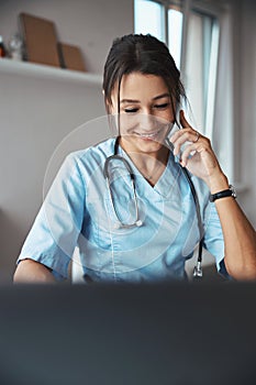 Cheerful female doctor having phone conversation at work