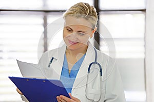 Cheerful female doctor is holding documents with patient information in office