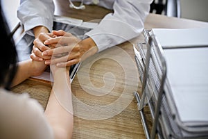 A cheerful female doctor holding a patient`s hands to reassuring during the meeting