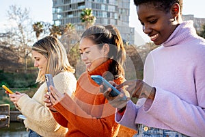 Cheerful female friends using cell phones and walking in the city. Technology addicted concept