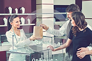 Cheerful female jeweler handing purchase in a shopping bag to he