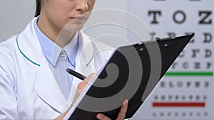 Cheerful female ophthalmologist filling patient examination data, diagnosis