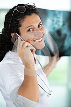 Cheerful female radiologist holding xray and using smartphone