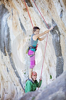 Female rock climber standing on shoulders of her partner in order to start climbing challenging route photo