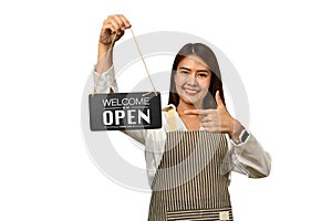 Cheerful female small business owner in apron holding OPEN sign and smiling to camera isolated on white background