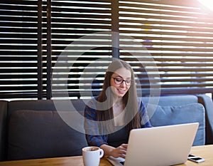 Cheerful female student working on notebook in cafe. Beautiful hipster girl using net-book