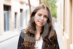 Cheerful female is walking in leather jacket on street outdoor