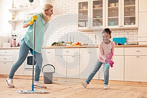 Cheerful foster daughter laughing while cleaning kitchen with mom