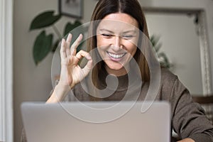 Cheerful freelance business woman showing OK hand gesture at laptop