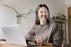 Cheerful freelance employee woman in wireless headphones sitting at laptop