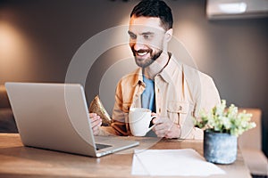 Cheerful freelancer man working from home. Attractive young man smiling, using his modern laprtop and talking by