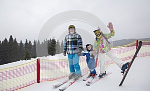 cheerful friendly family of three stands on the ski slope, parents and son in ski equipment