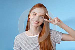 Cheerful friendly gorgeous redhead girl glancing happily show peace victory sign tilting head cute smiling broadly white