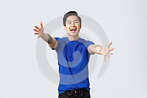 Cheerful friendly-looking young male student, asian man in blue t-shirt with tattoos, reaching hands towards camera for