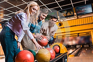 Cheerful friends choosing bowling balls in