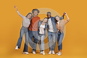 Cheerful friends embracing and celebrating on orange background