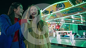 Cheerful friends having fun at night amusement park. Happy girls laughing walk