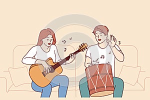 Cheerful friends playing musical instruments, sitting on sofa and using drum with guitar