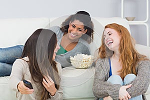 Cheerful friends with remote control and popcorn bowl at home