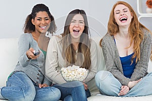 Cheerful friends with remote control and popcorn bowl on sofa