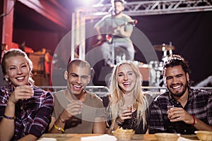 Cheerful friends sitting side by side with musician in background