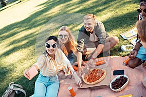 Cheerful friends taking selfies and eating pizza.