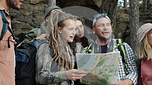 Cheerful friends tourists studying map then walking in green autumn forest