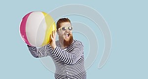 Cheerful funny guy in sunglasses playing with beach inflatable ball on pastel blue background.