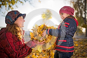 Cheerful and funny mother plays with yellow maple leaves