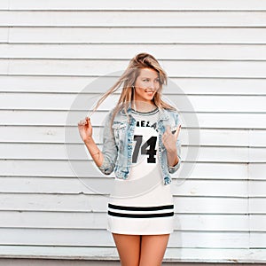 Cheerful funny young woman in American style clothes near the white wooden house. Charming girl enjoys a warm sunny day.