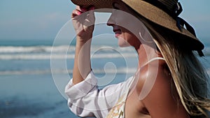 Cheerful girl in bikini and sun hat walking along the ocean coast