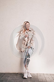 Cheerful girl with bionic prosthesis stands near the wall in the street