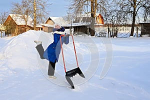 cheerful girl cleans snow with shovel in countryside. Girl laughs and dances. Teenage girl with large scraper helps adults to